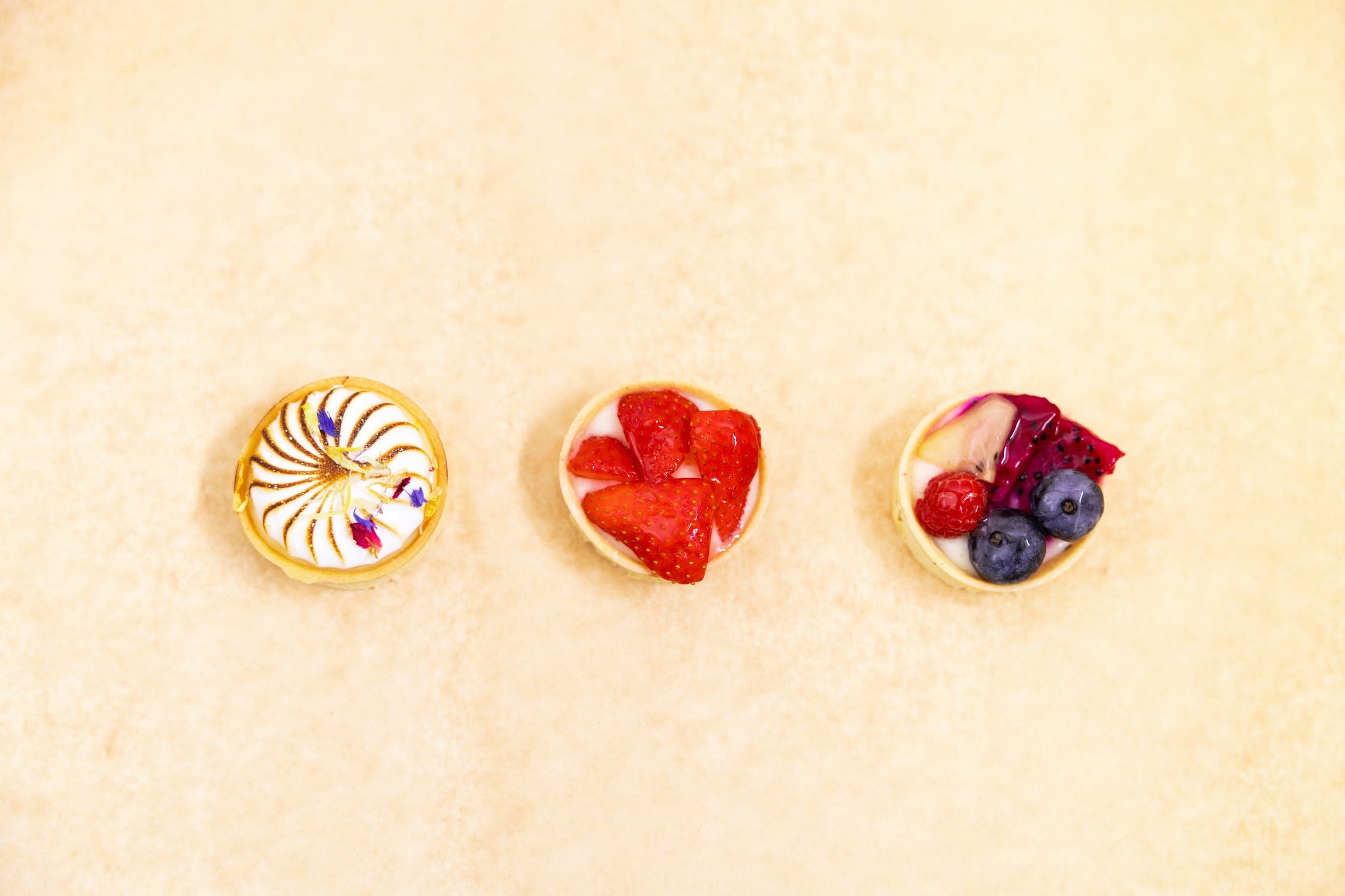Drei Tartelettes mit Baiser, Erdbeeren und Beeren nebeneinander angerichtet