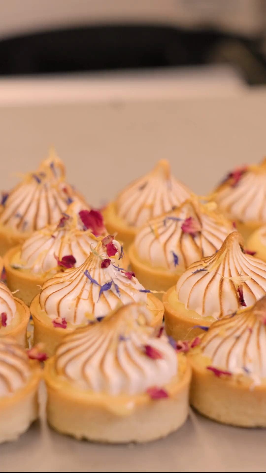 Baiser-Tartelettes mit essbaren Blüten, dicht an dicht auf einem Blech in der Backstube