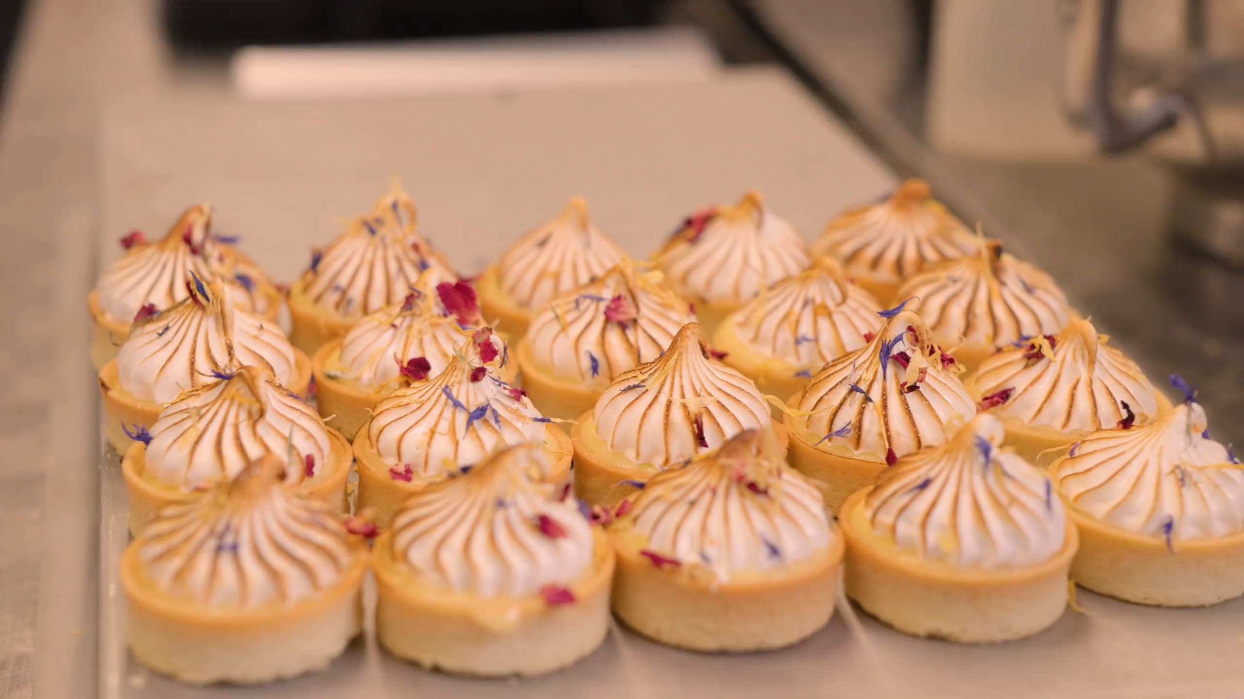 Baiser-Tartelettes mit essbaren Blüten auf einem Blech in der Backstube